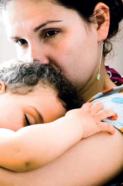 Mother is holding her sleeping baby. She looks concerned and worries